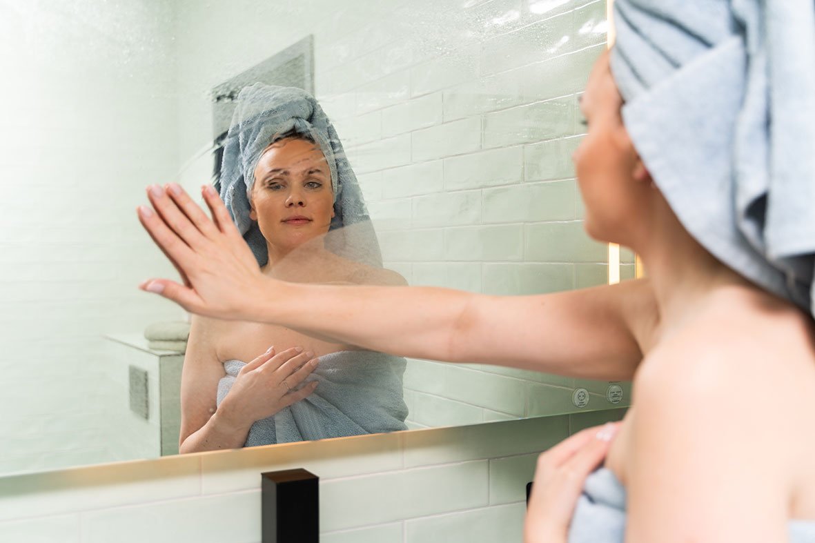 Person tørker dugg av speil på bad etter dusj, som viser behov for god ventilasjon.