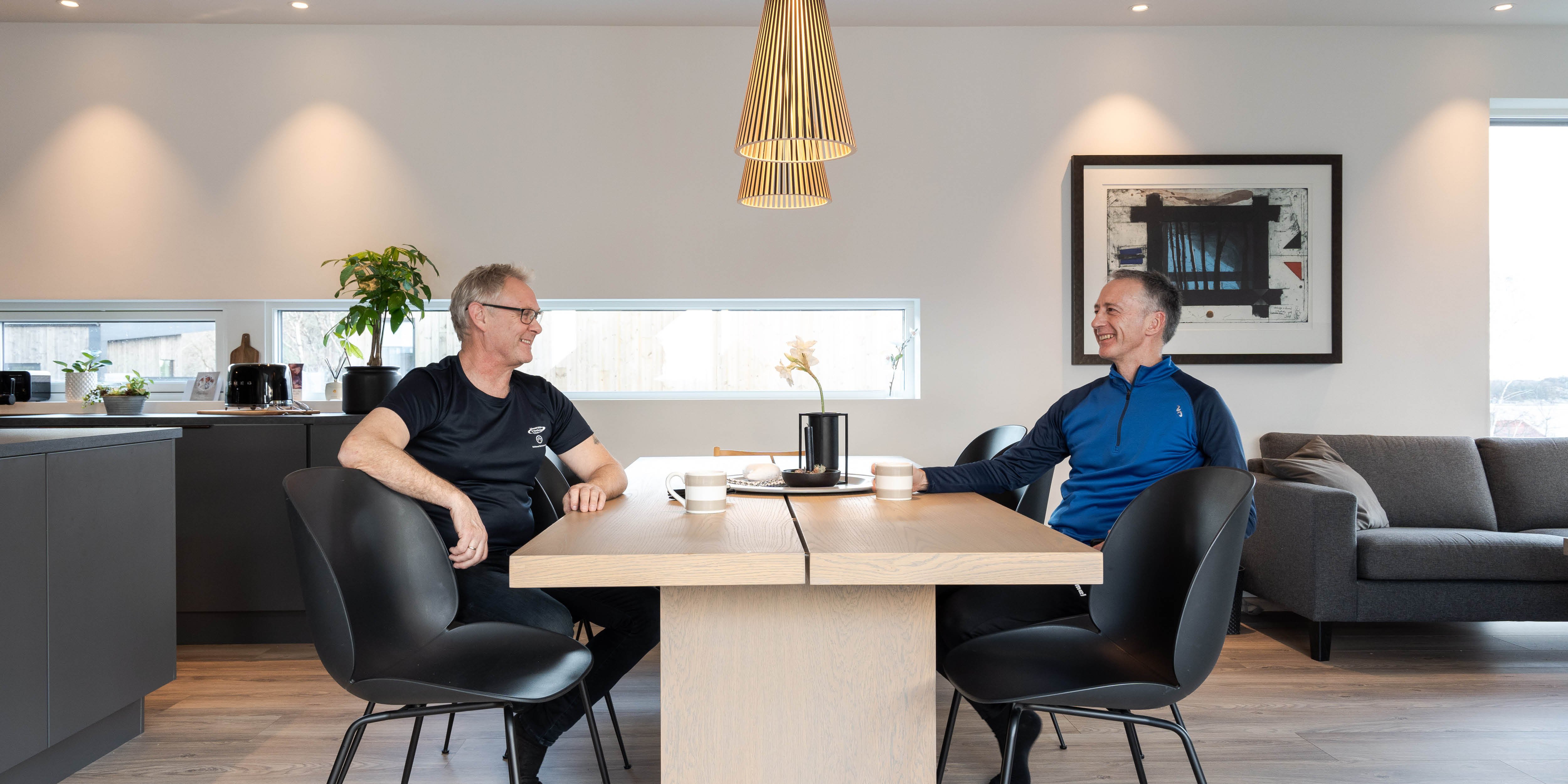 To naboer sitter ved spisebord i en moderne stue med åpen kjøkkenløsning