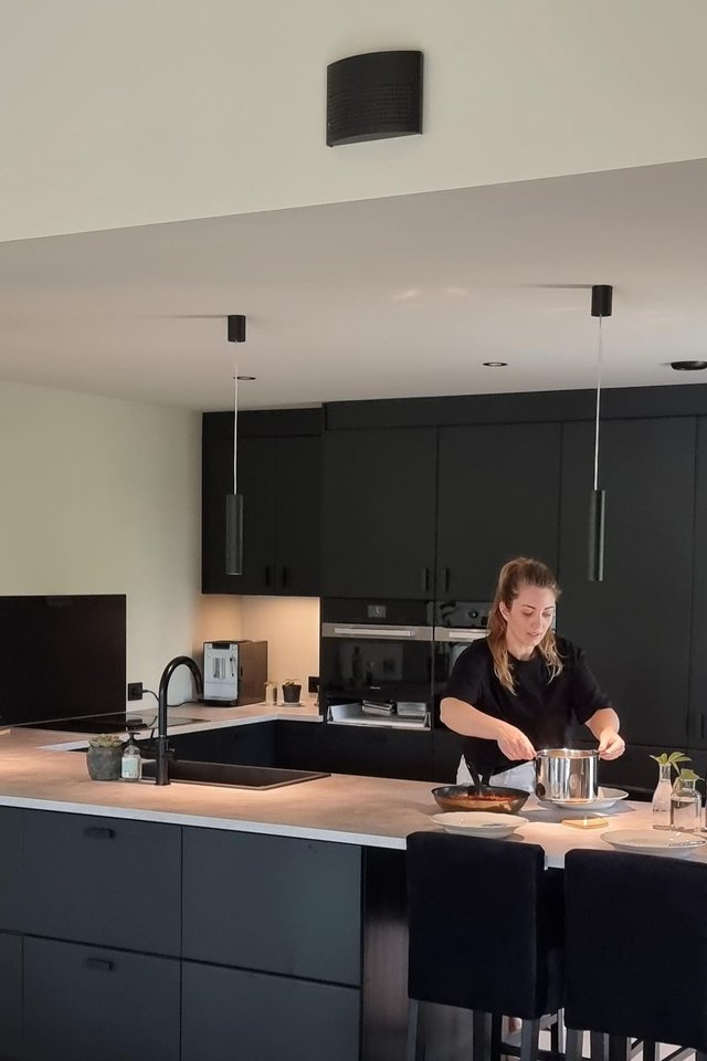 Moderne kjøkken med kjøkkenøy, integrerte skap og person som lager mat i åpen bolig.