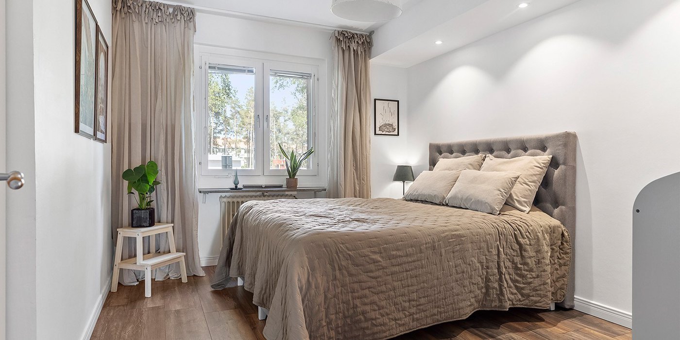 Lyst soverom i renovert leilighet med dobbeltseng, tregulv og vinduer med dagslys.