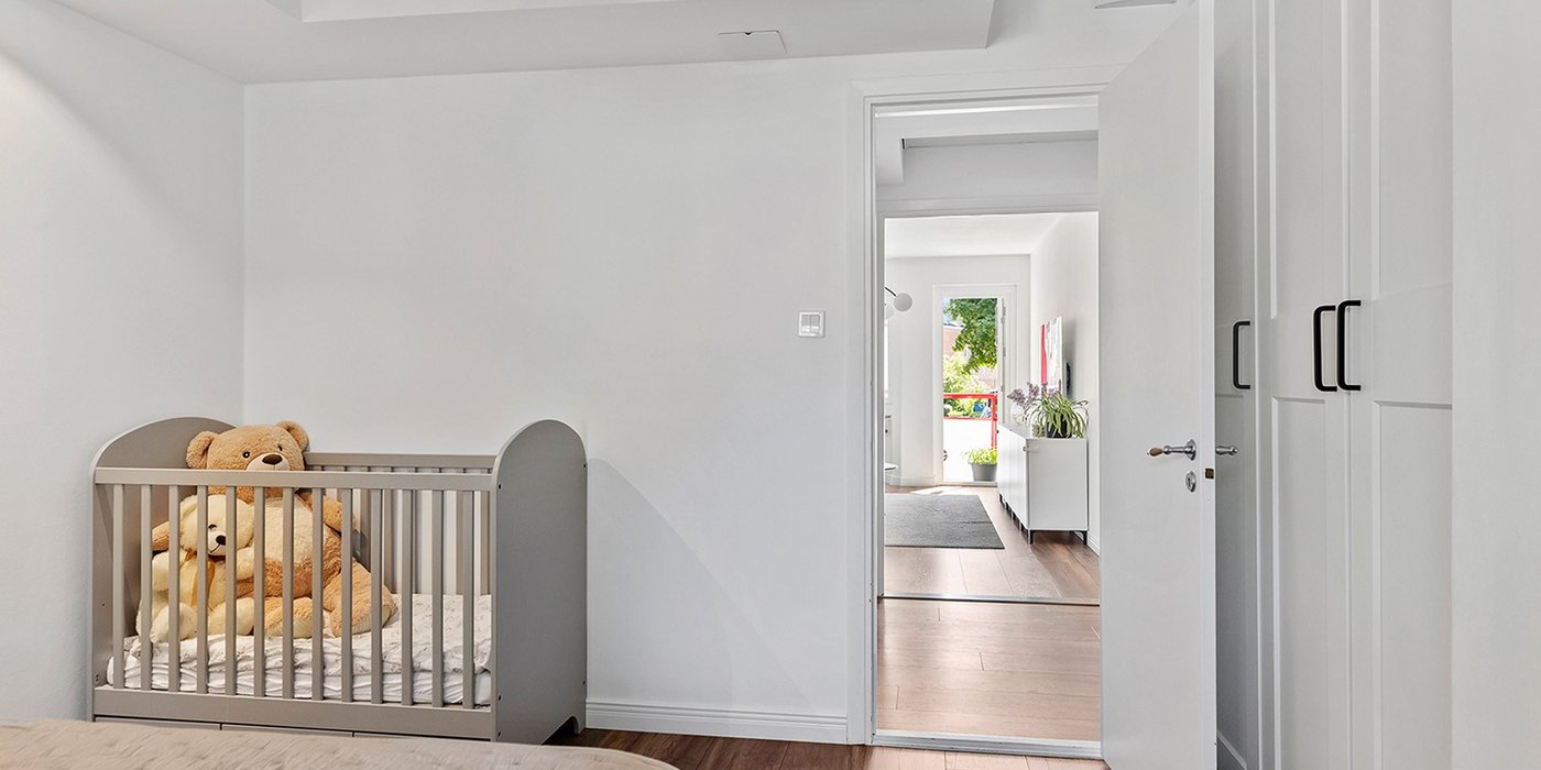 Soverom i renovert leilighet sett fra døråpning, med seng, tregulv og gjennomgang til gang.