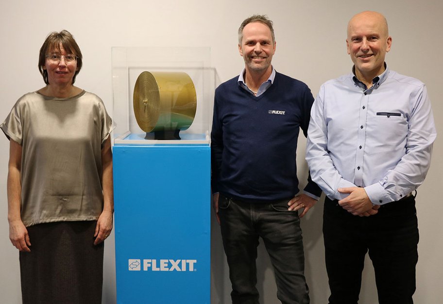 Tre personer står ved siden av en Flexit-utstilling med Stage Wheel lakkert i gull.