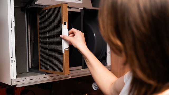 The filter is being removed from the air handling unit as part of routine maintenance. The image shows proper handling of the filter frame and easy access to the service compartment.
