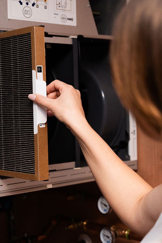 Person tar ut ventilasjonsfilter fra et Flexit ventilasjonsaggregat for vedlikehold.