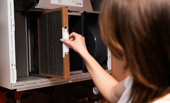 The filter is being removed from the air handling unit as part of routine maintenance. The image shows proper handling of the filter frame and easy access to the service compartment.
