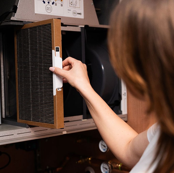Hånd setter inn ventilasjonsfilter i åpent Flexit ventilasjonsaggregat under service eller vedlikehold.