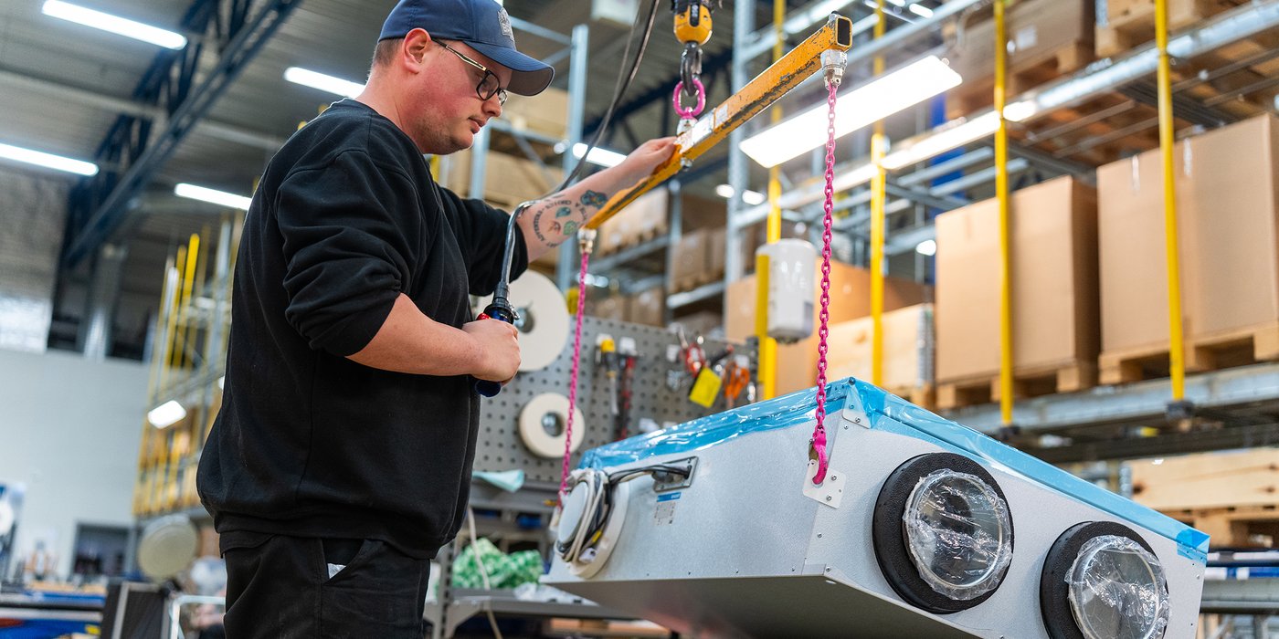 Medarbeider som håndterer Flexit ventilasjonsaggregat under montering i produksjons- og lagerområde.