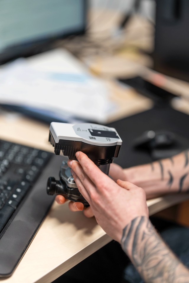 Hånd justerer måleinstrument på et skrivebord, brukt til teknisk arbeid.