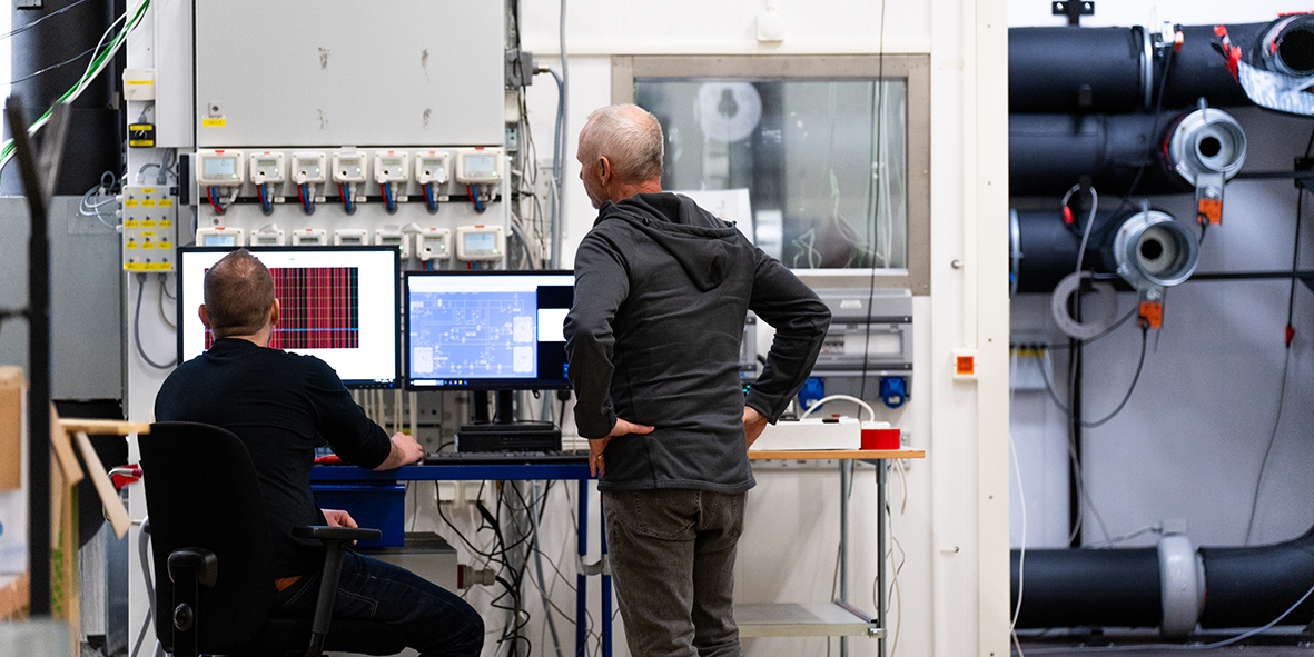 To fagpersoner tester ventilasjonsaggregat i Flexits laboratorium med måleutstyr og tekniske installasjoner.